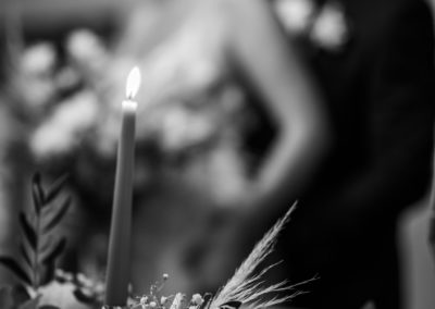 Reportage de la découverte de la salle du mariage après le cocktail. Les mariés sont floutés et en arrière plan. On voit en premier plan en bas les décorations de la table. La photo est noir et blanc et très contrastée. Les mariés sont l'un derrière l'autre.