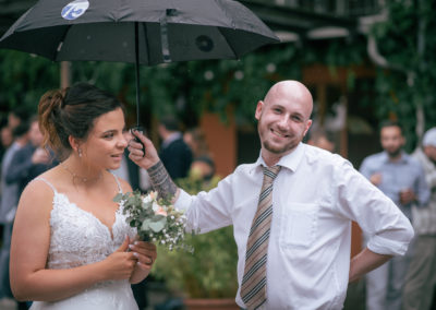 Reportage après la cérémonie du mariage quand il pleuvait légèrement. Un invité tient le parapluie de la marié et rigole.